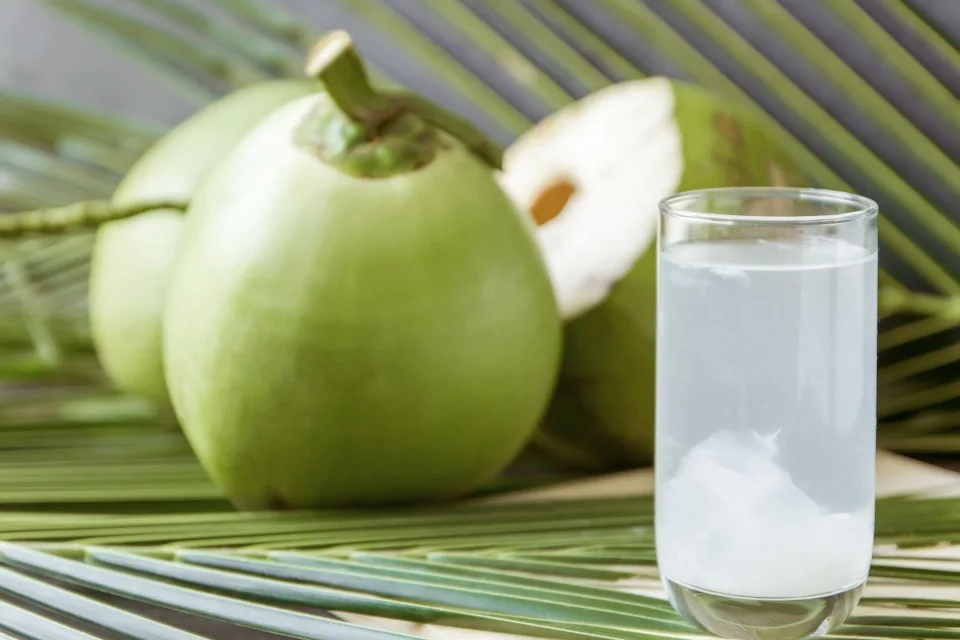 Ly nước dừa tươi mát trên bàn gỗ, giúp da sáng và giữ ẩm tự nhiên