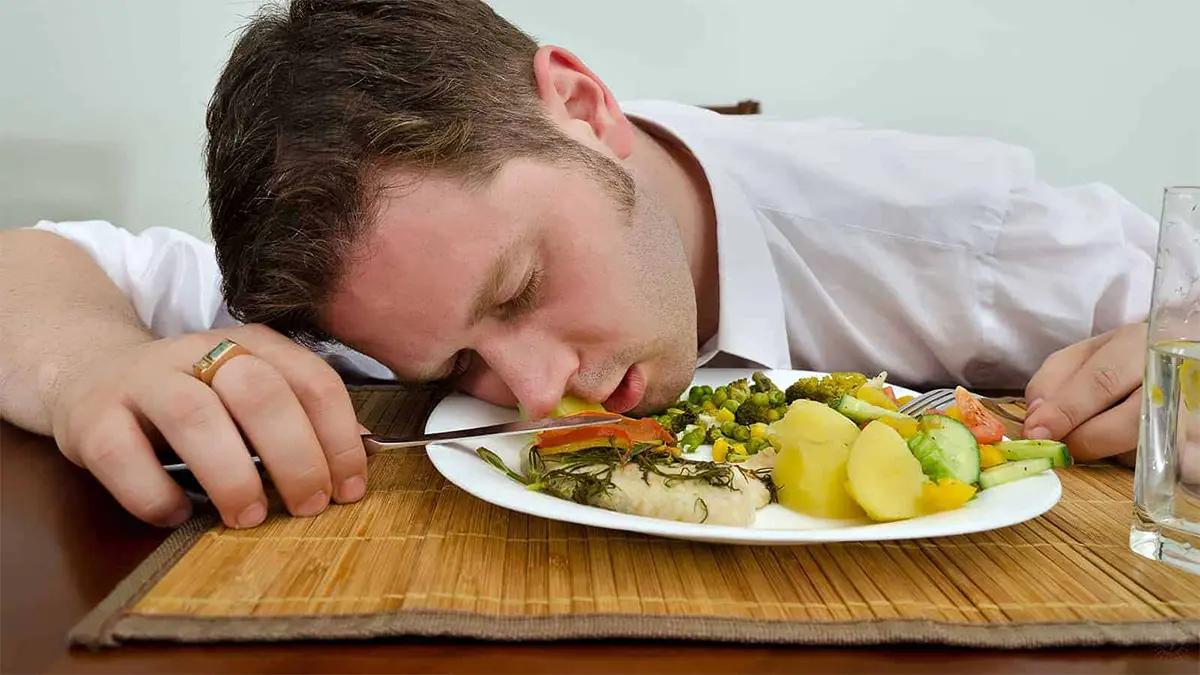 Người mệt mỏi ôm đầu trước bàn ăn đầy đồ ngọt và thức ăn nhanh